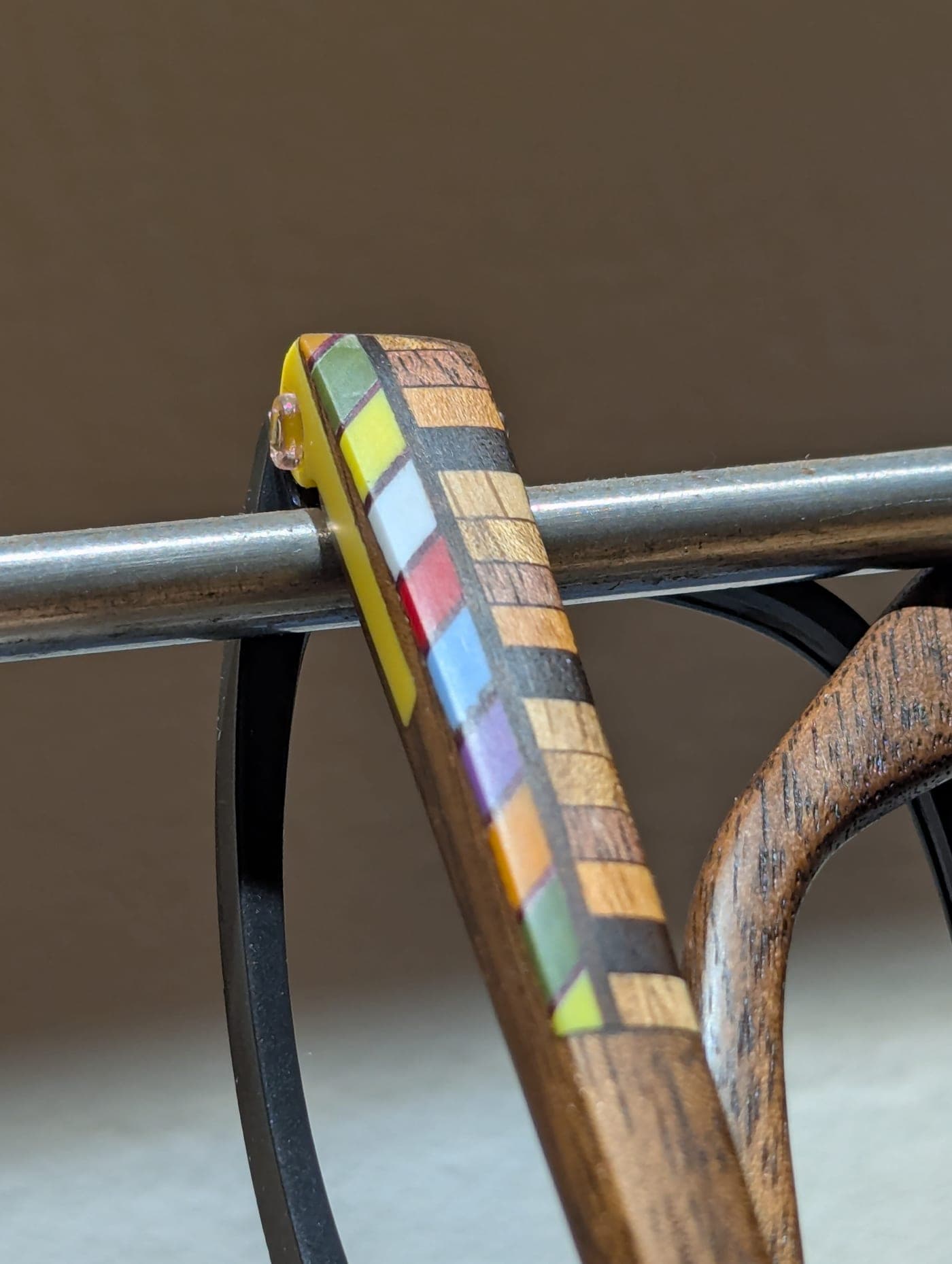 Close-up of a wood temple with checkerboard mosaic inlay resting on a metal workbench fixture